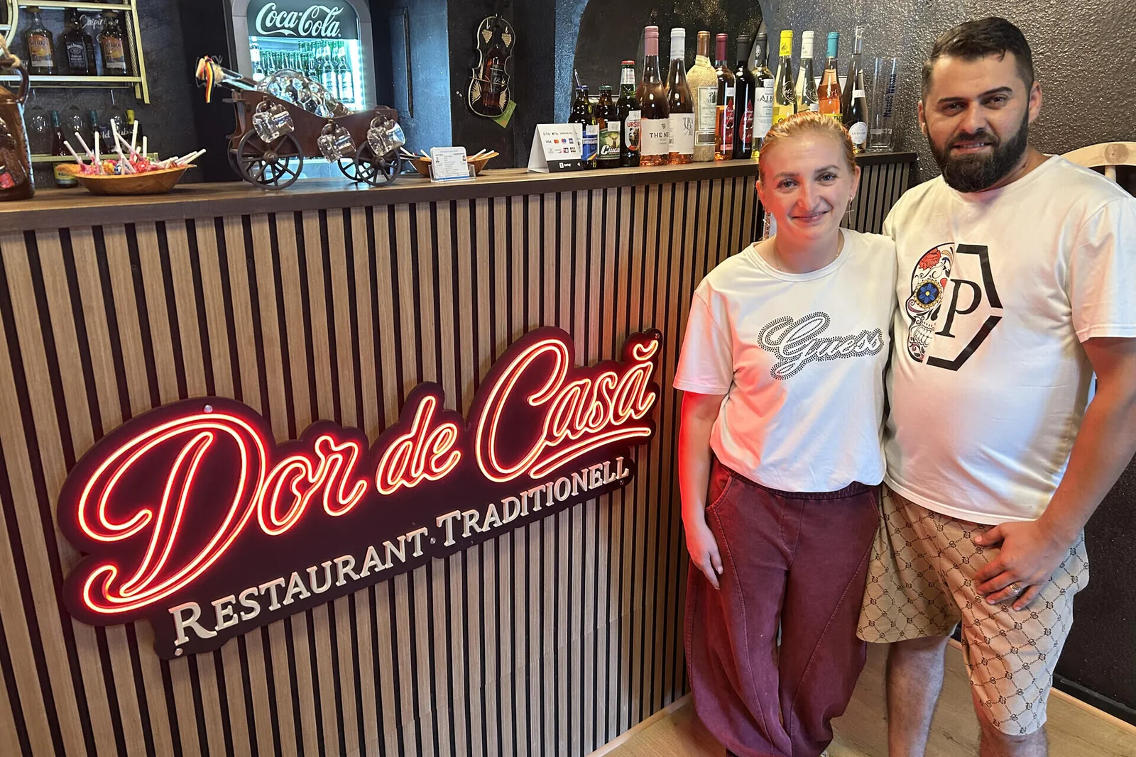 Die Gastgeber von Dor de Casă vor der Leuchtschrift an der Theke des Restaurants